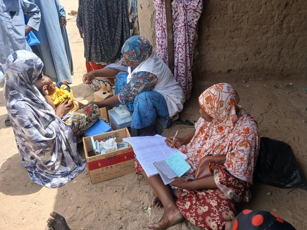 Agents de santé remplissant un registre assis au sol avec une glacière de vaccins
